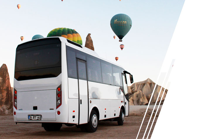 A white coach bus is parked overlooking an area with hot air balloons