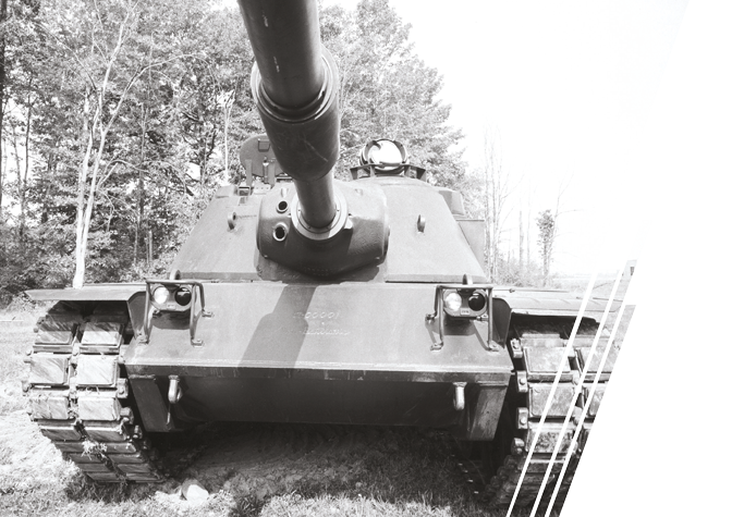A black and white image of a battle tank in front of a bank of trees.