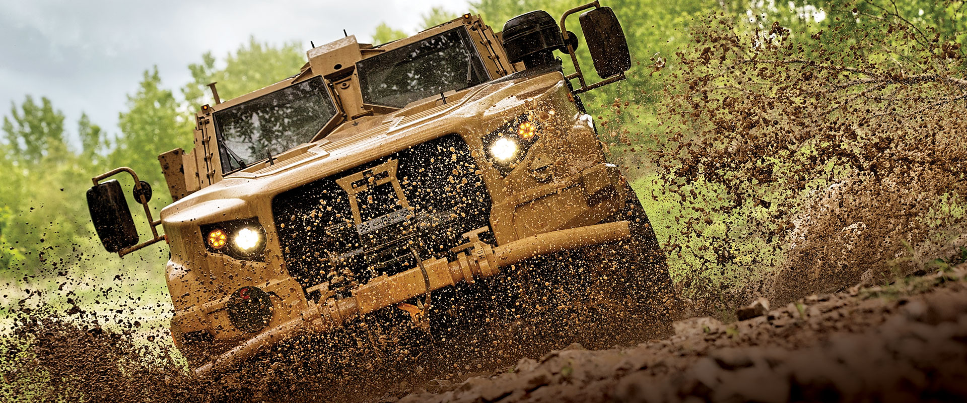 Wheeled defense vehicle going through a stream of mud.