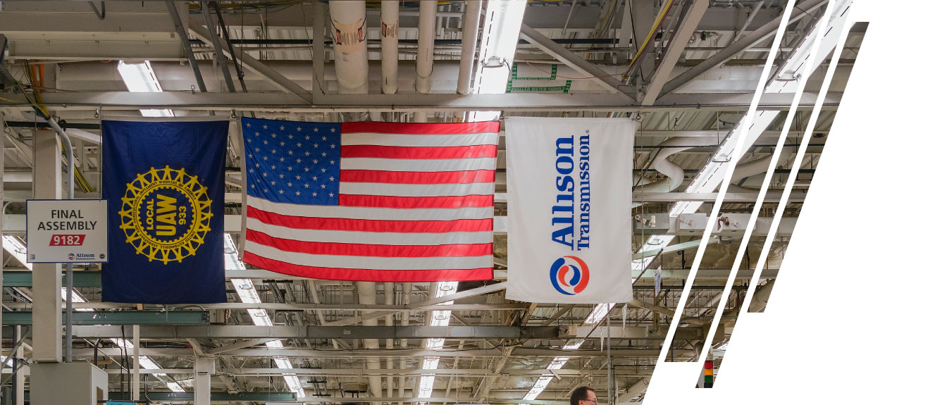 The United Auto Workers (UAW), the United States of America and the Allison Transmission flag hang in a manufacturing plant.